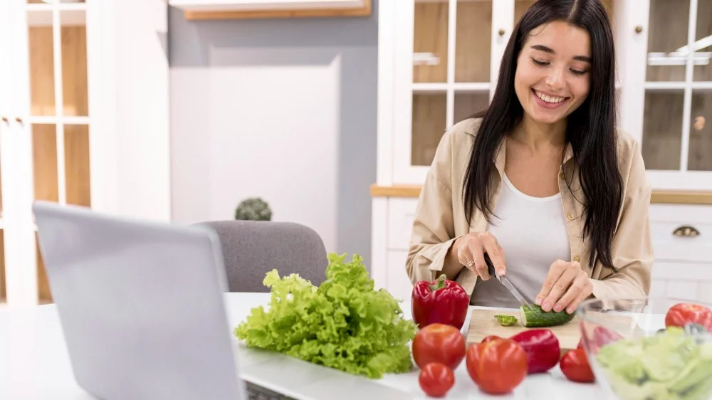 Woman chopping vegetables in her kitchen with a laptop open